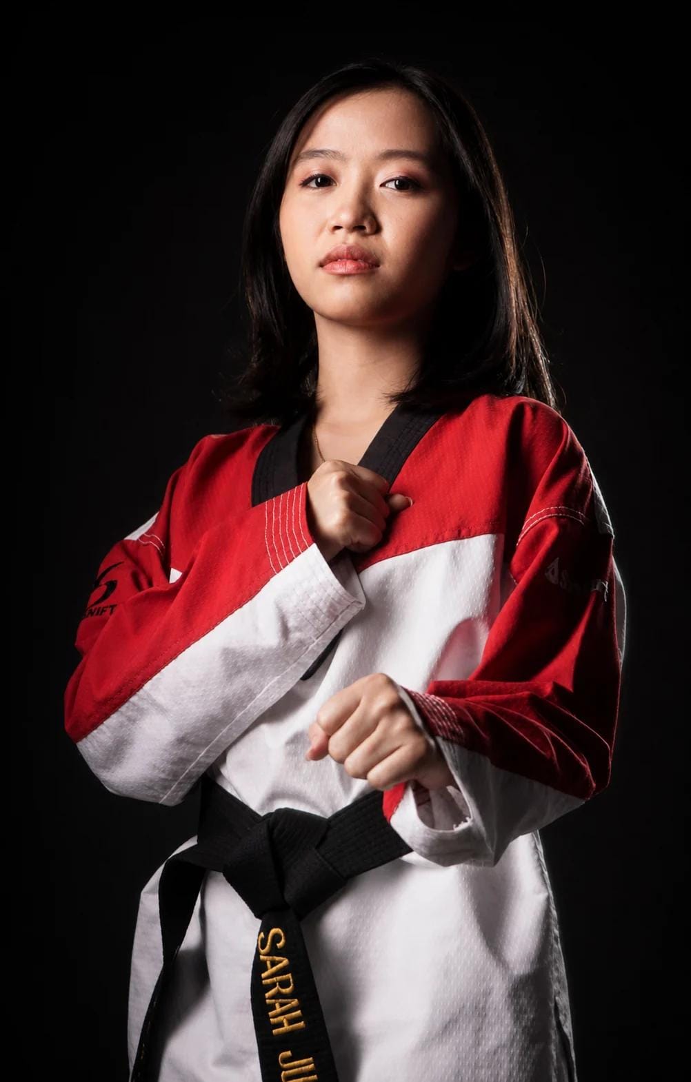 Coach Sarah in a red-trimmed dobok, holding a fist at her chest
