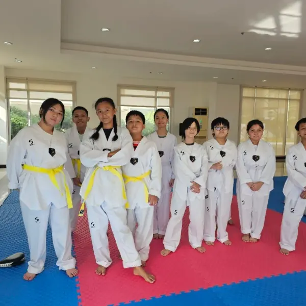 Ten students in dobok and yellow belts standing together on the blue and red mat
