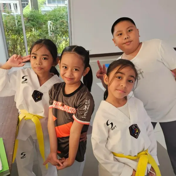 Four young students in white dobok, two flashing peace signs at the camera before class